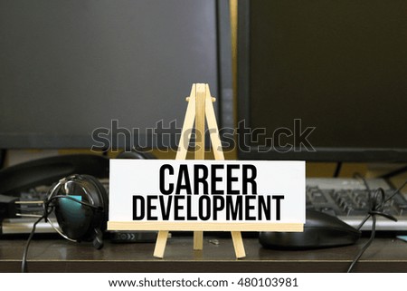 conceptual image, word CAREER DEVELOPMENT on white frame and wooden tripod stand with background monitor, head phone, mouse and keyboard on the table. Technical concept.  