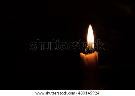 One light candle burning brightly, image is isolated against a black background and fades into a shadow.