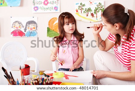 Child with teacher draw paints in play room. Preschool.