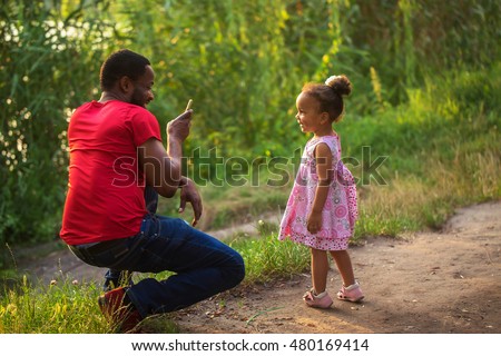 Black African father takes photo of his daughter with by means of mobile phone.