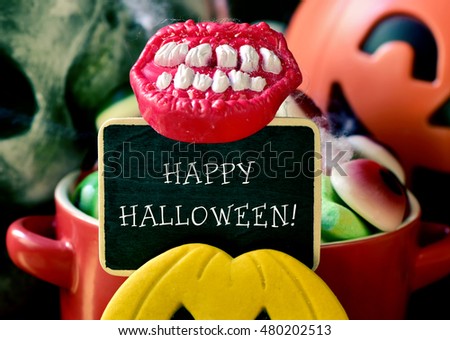 the text happy halloween written in a chalkboard, different Halloween candies and cookies, and some scary ornaments, such as a skull or a carved pumpkin