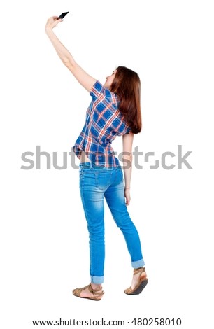 back view of standing young beautiful woman using a mobile phone. Girl in a plaid shirt is cancer and makes selfie.