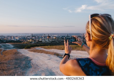 Cropped image of young woman tourist use mobile phone taking photo outdoor. Blurred view hill, city and sea on a background. 