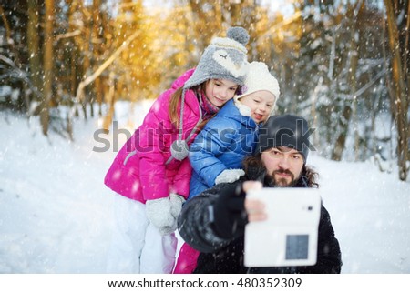 Two cute little sisters taking a selfie with their father on snowy winter day