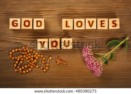 Inscription "God loves You" on wooden blocks with rosary and flower