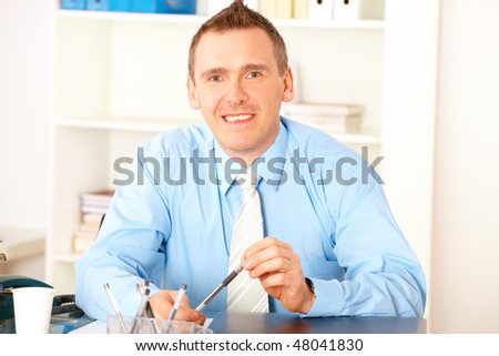 Happy businessman sitting at desk in office with pen in hands