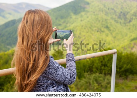 Beautiful young woman with beautiful hair is doing a photo on her black phone of peaceful nature.