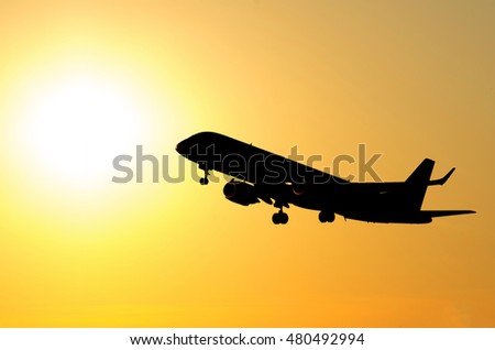 Commercial airplane taking off against orange sunset background