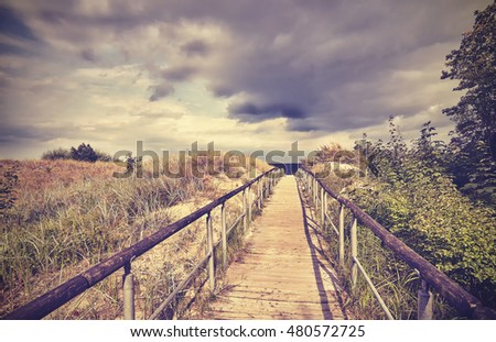 Vintage toned wooden footpath leading to a beach, rainy clouds in distance.