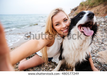 Cheerful cute young woman taking selfie with dog on the beach