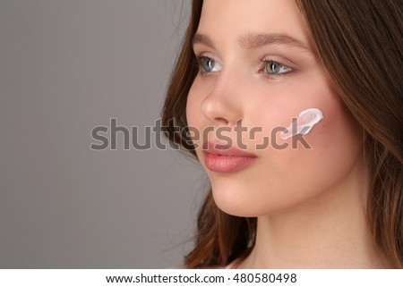 Girl with cream on her face. Close up. Gray background