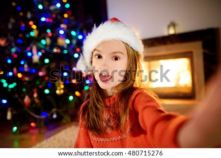 Happy little girl taking a selfie by a decorated Xmas tree on Christmas eve
