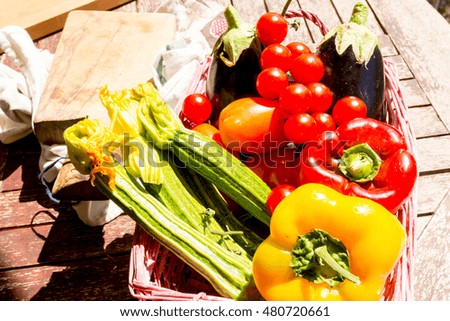 Zucchini, eggplant, peppers and tomatoes in a basket on a wooden board. Cooking with vegetables and greens
