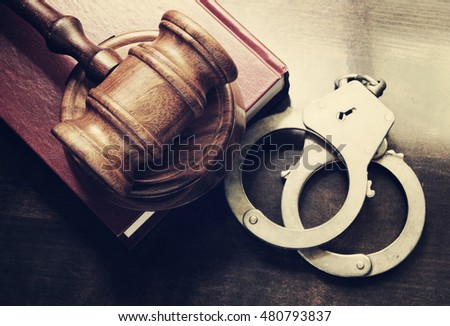 Gavel and handcuffs with red legal book on wooden table Royalty-Free Stock Photo #480793837