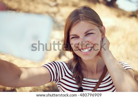 Pretty smiling woman taking picture of herself over rural background outdoors. Concept of summer holidays and travel. 