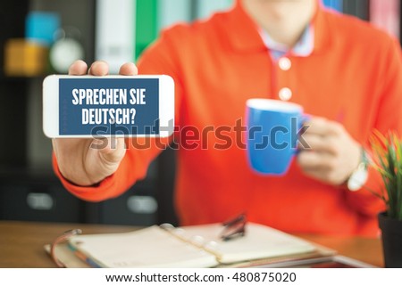 Young man showing smartphone and SPRECHEN SIE DEUTSCH? word concept on screen