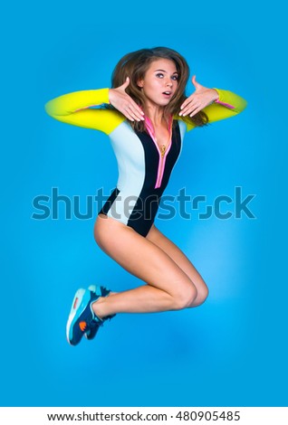 One happy attractive gorgeous young fit modern woman in sportswear working out, dancing, jumping with joy, full length, studio image on blue background