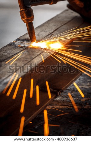 Welder in workshop manufacturing metal construction by cutting to shape using huge orange sparks