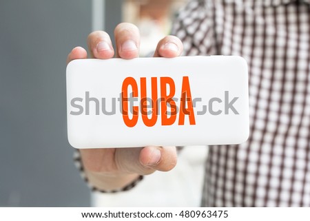 Man hand showing CUBA word phone with  blur business man wearing plaid shirt.