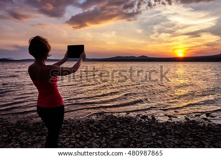Girl photographing the sunset on the table, summer