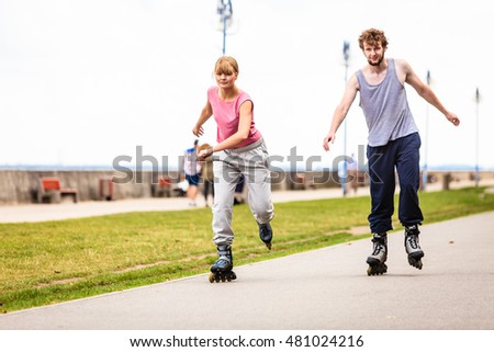 Active young people friends in training suit rollerskating outdoor. Woman and man riding enjoying sport.