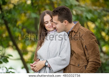 Romantic couple relaxing in autumn park, cuddling, kissing, enjoying fresh air, beautiful  nature, nice fall weather. Beloved spending time together. Yellow leaves in background