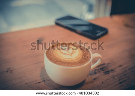 Vintage tone,a white cup of coffee Cappuccino with art tulip style and mobile phone on wooden table