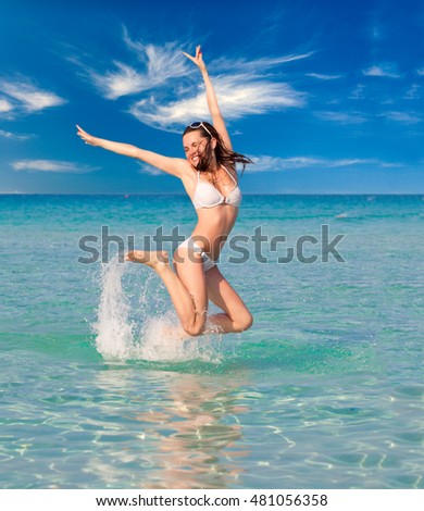 Laughing woman in white bikini jumping in the sea on a sunny day