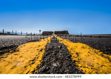 Yellow road dividing lines from low perspective along coastal road leading towards hills