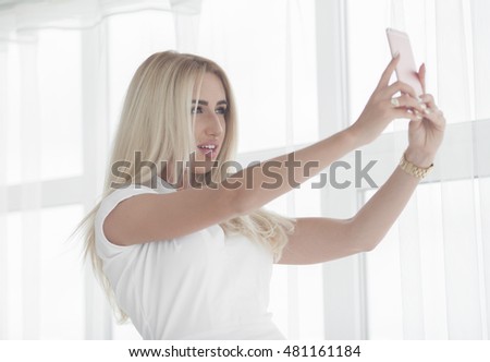 Beautiful smiling blonde business woman in white dress photographing selfie on a phone in her hands outdoors. copy space