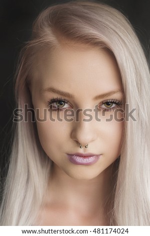 Alternative young female model with blonde hair and piercings in her nose on a black background. teenage girl. Skin care concept.