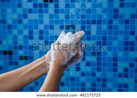 Washing hands with soap and a sponge under running water, shower in bathroom, mosaic