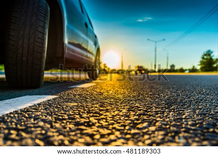 Sunset in the country, the headlights of the approaching car. Wide angle view of the level of a parked car wheels, image in the blue tones