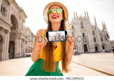 Young female tourist showing phone with photo standing in front of the famous Duomo cathedral in Milan