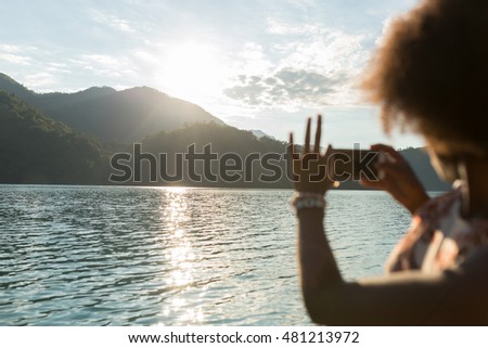 Wonderful sunset over hills, tourist taking a picture of the lake. Afro american woman visiting Europe.