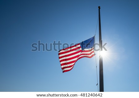 American flag lowered to half mast backlit by bright sun lens flare