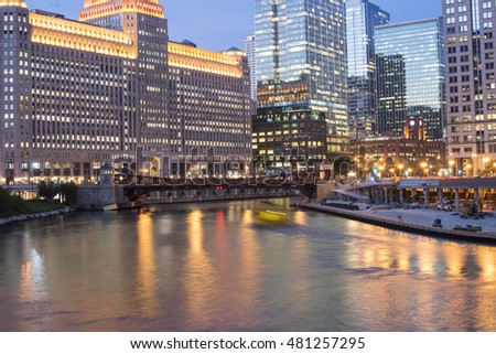 Chicago River with urban skyscrapers illuminated with lights and water reflection at dusk