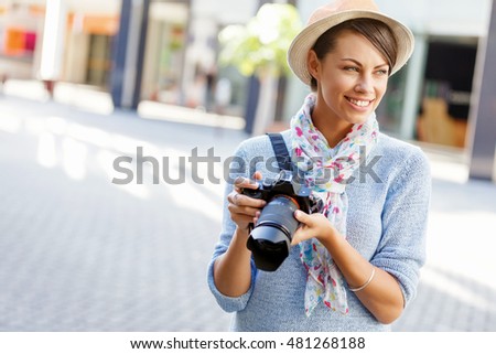 Outdoor summer smiling lifestyle portrait of pretty young woman with camera