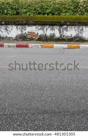 Asphalt road with yellow red and white traffic sign at sidewalk curb and old white concrete fence