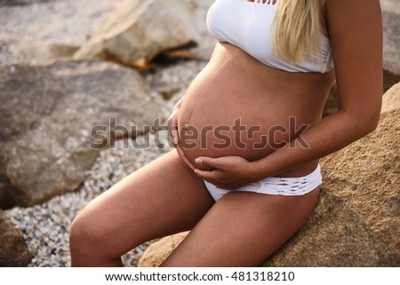 Closeup picture of belly of pregnant girl over swimming pool with blue water