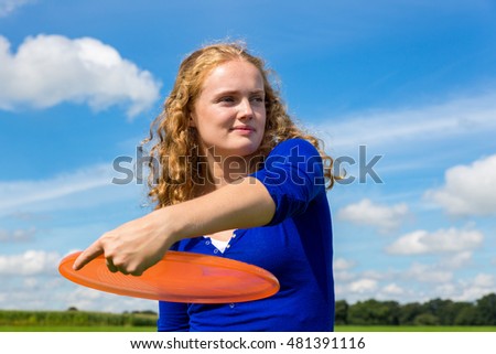 Young caucasian woman holding orange frisbee outdoors against blue sky