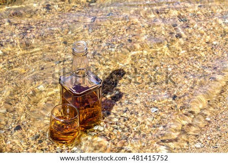Bottle and a glass of whiskey are cooled in a mountain river
