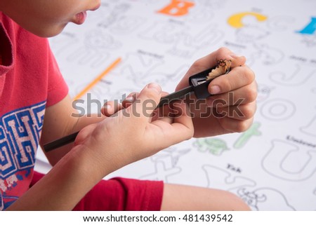 Little child boy using sharpener for pencil shaving his color pencil
