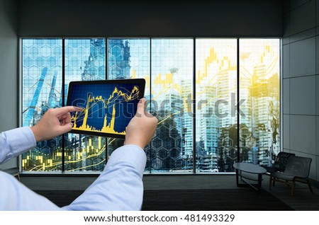 Fintech Investment Financial Internet Technology Concept. Man hand holding tablet with stock market chart graph screen .Window showing smart building and graph chart background