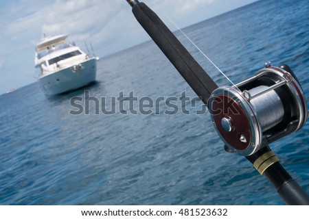 Fishing rod on a boat over blue sky and white sailing boat in the sea. Picture of fishing rod in pole holders on the back of a boat