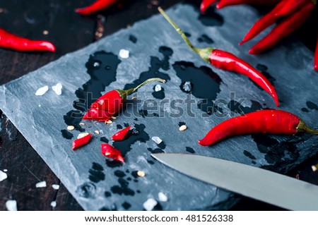 Slicing Chilli pepper with Knife on kitchen board on wooden background.