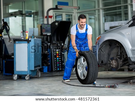 Smiling mechanic pushes the tire in a workshop Royalty-Free Stock Photo #481572361