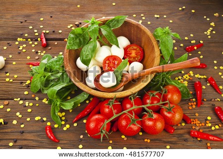 Caprese salad in a wooden bowl with tomatoes and basil on a wooden background