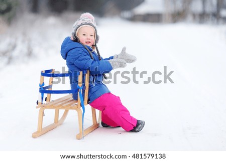 Funny little girl having fun with a sleight in beautiful winter park