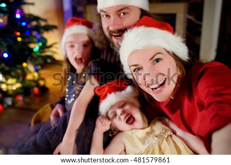Young happy family of four taking a photo of themselves by a fireplace in a cozy dark living room on Christmas eve